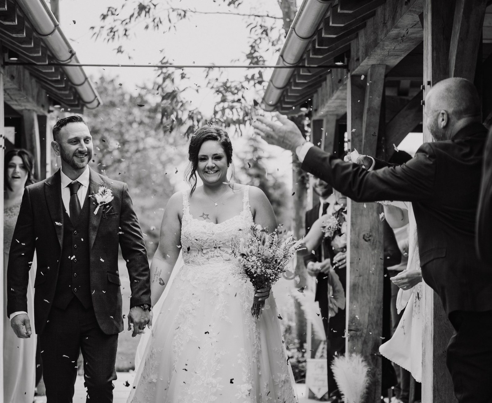 Bride and groom walking out through a shower of confetti, in black and white