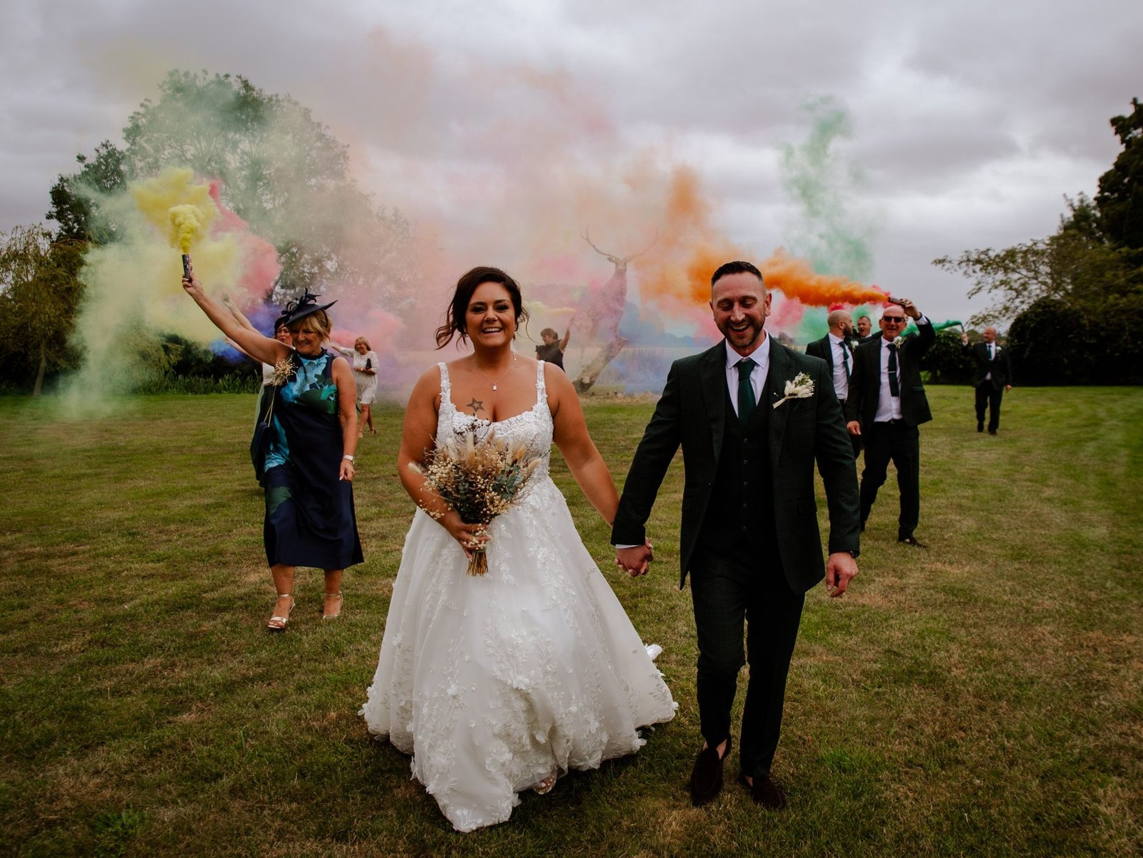 Couple walking hand in hand as guests set off coloured smoke behind them